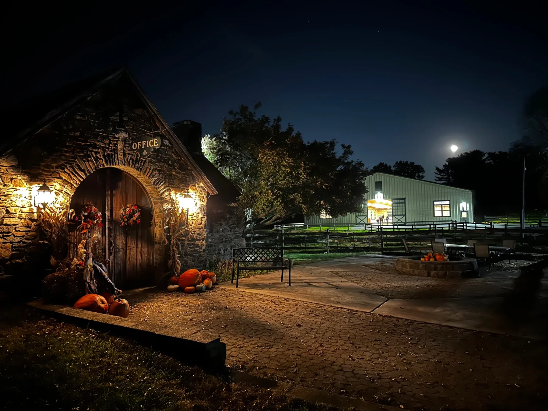 Shadow Creek Farm’s stone office and arena glowing in the evening, with pumpkins beside the doorway