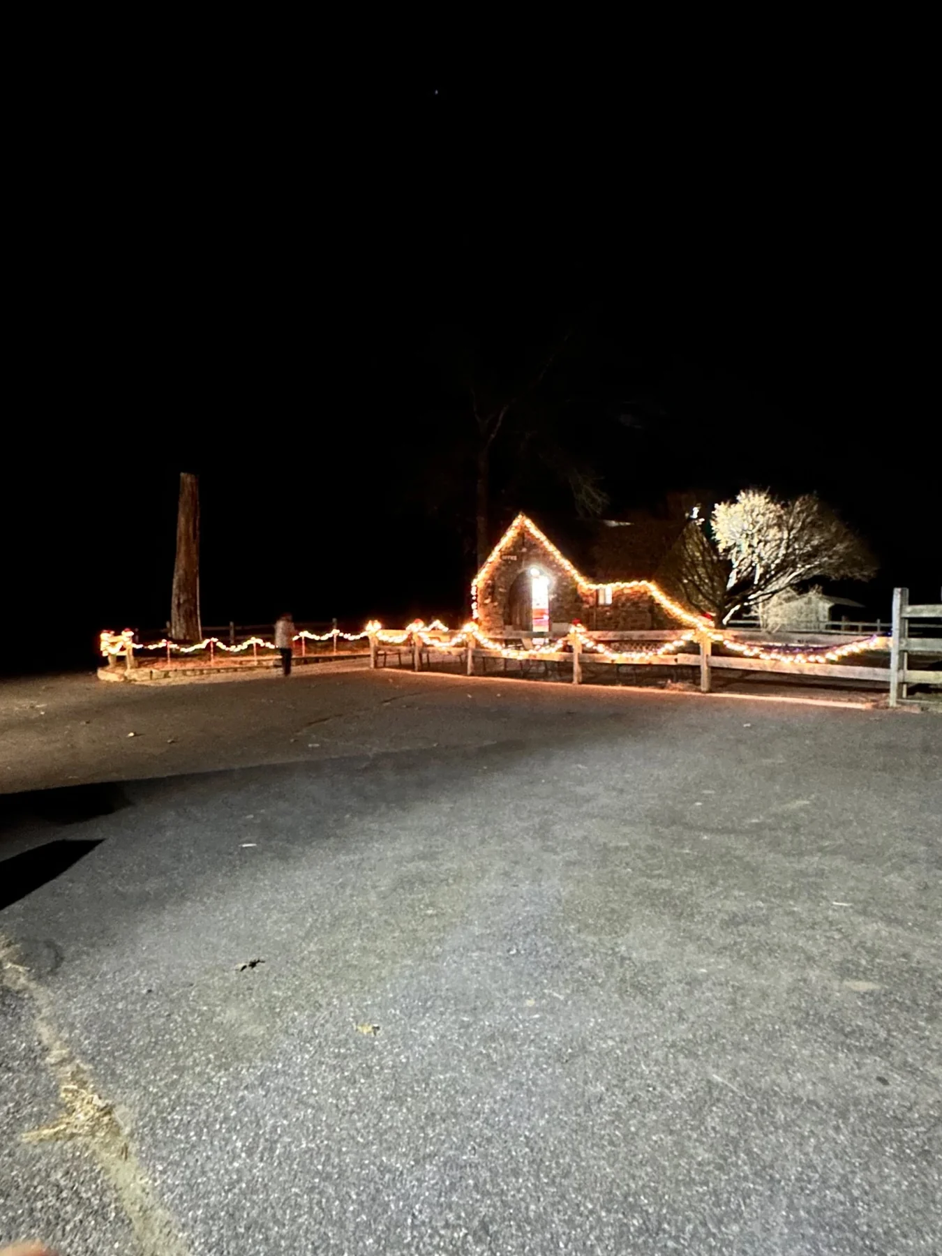 Warm Christmas lights outlining the stone barn and courtyard fences after dark