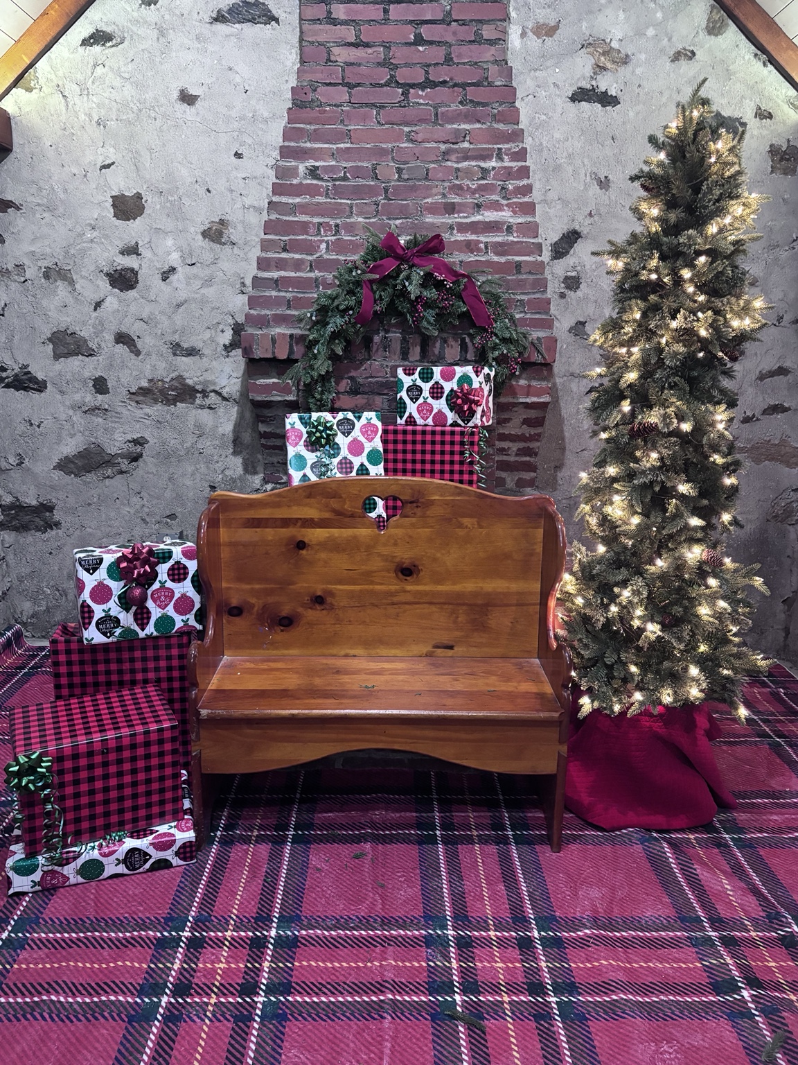 A wooden bench surrounded by wrapped presents, a wreath and a glowing Christmas tree at the farm
