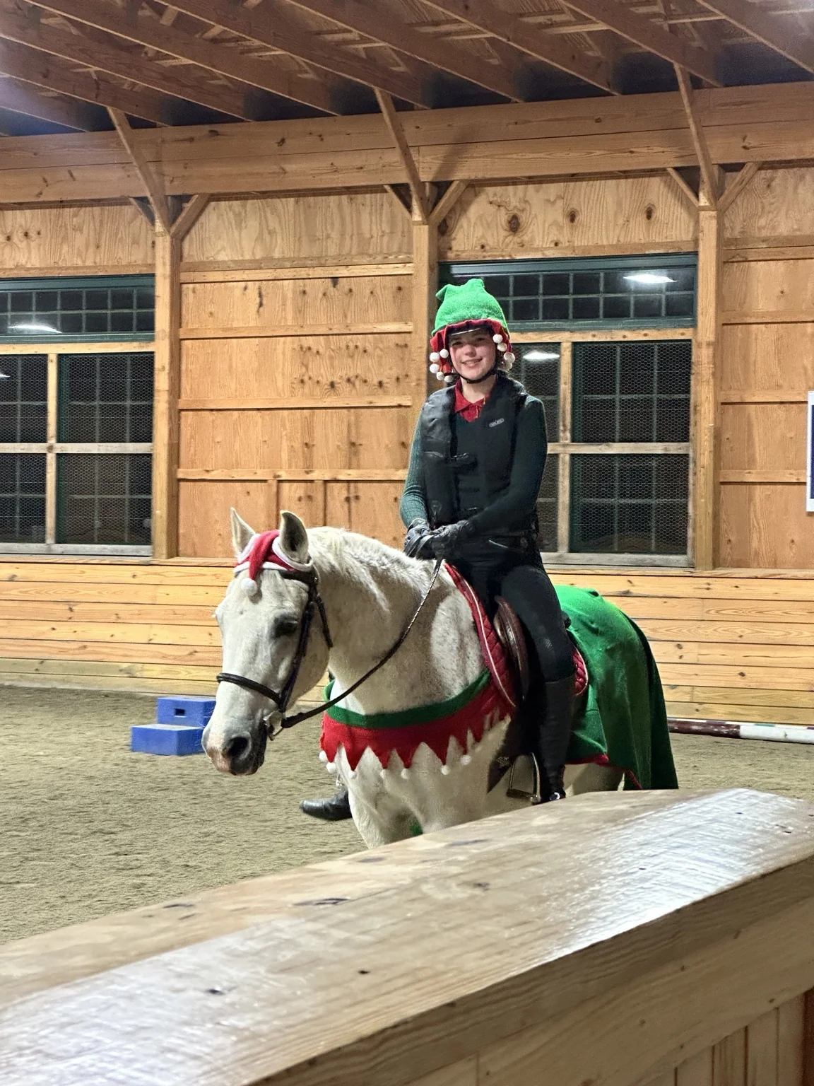 A rider in an elf hat on a grey pony wearing red and green holiday decorations