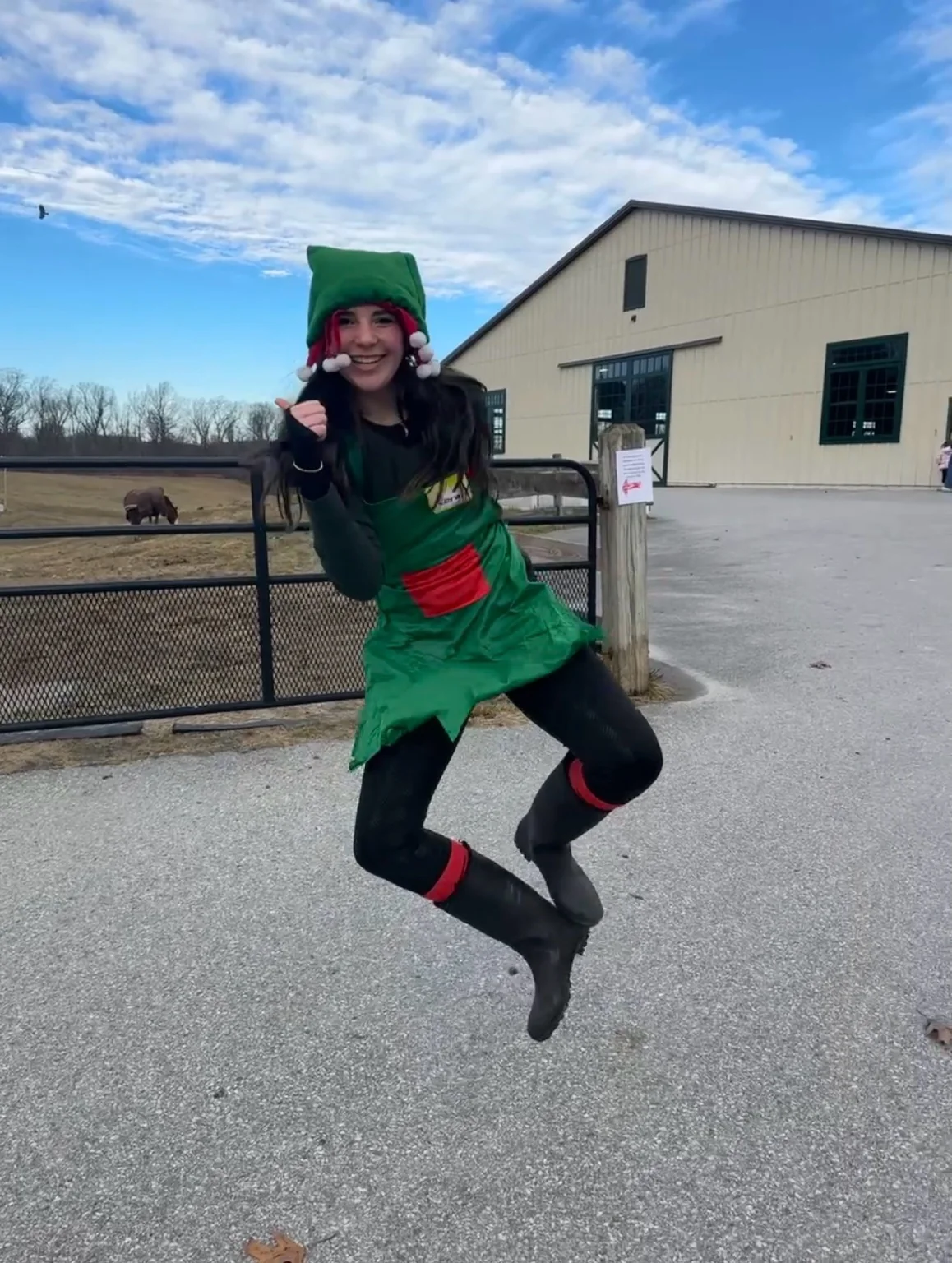 A smiling helper in an elf costume jumping beside the farm arena