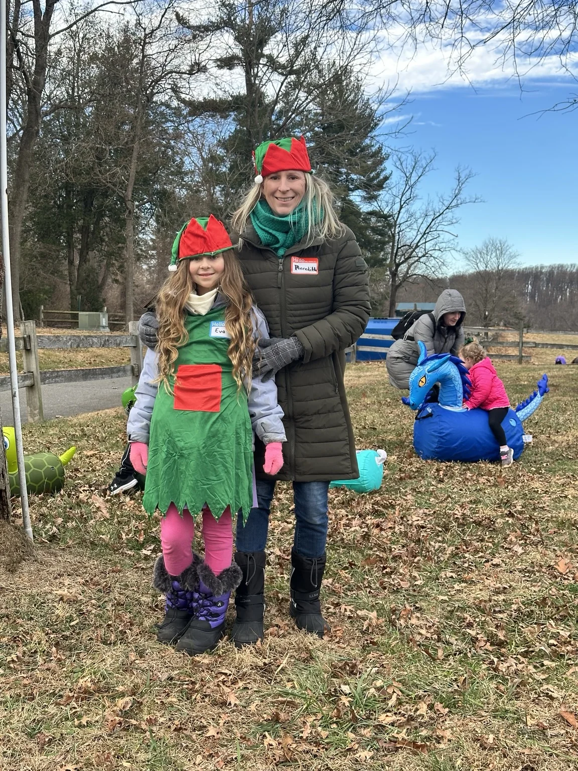 Two smiling holiday helpers in red and green elf hats outdoors at the farm
